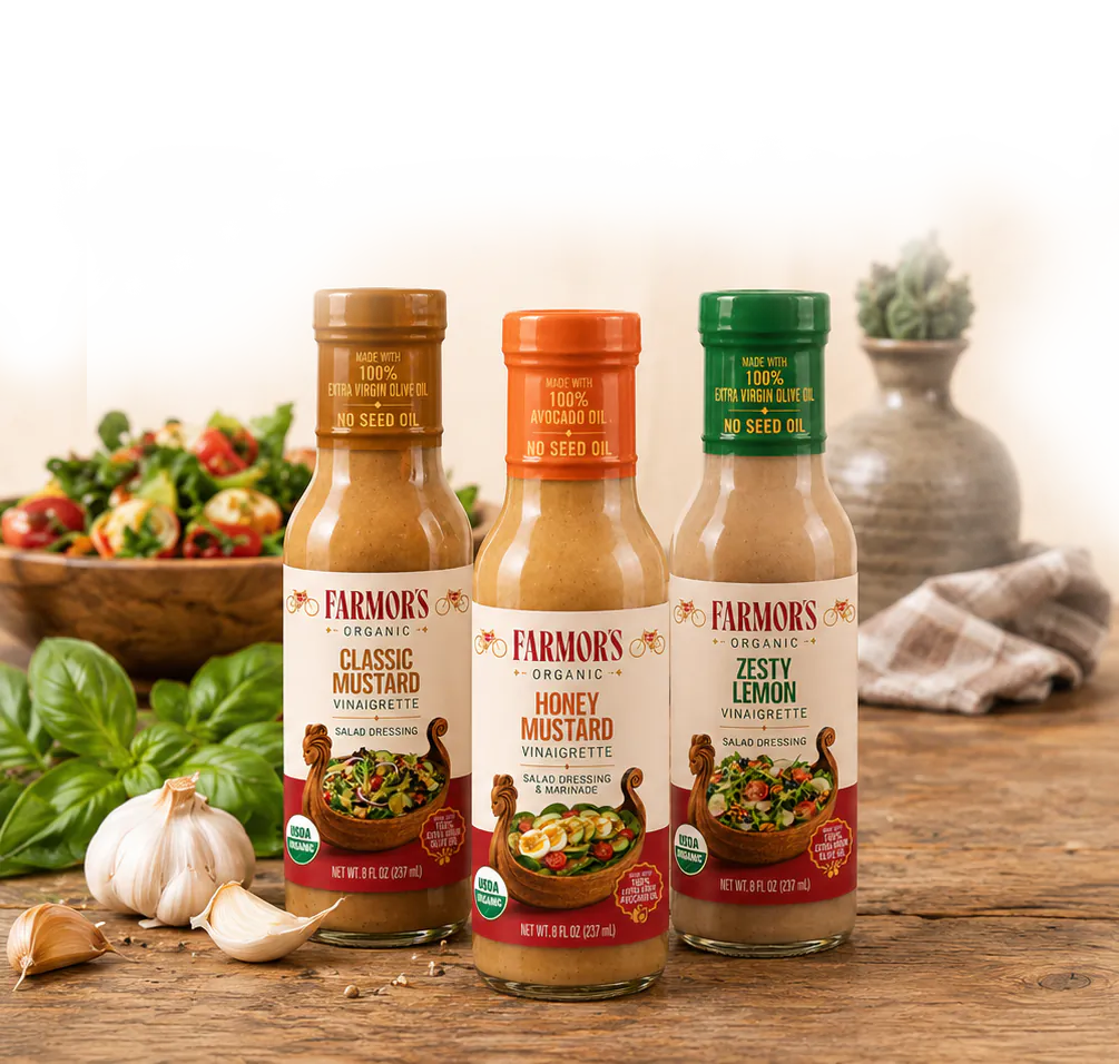 Three Farmor’s dressing bottles on a rustic kitchen surface with herbs and garlic