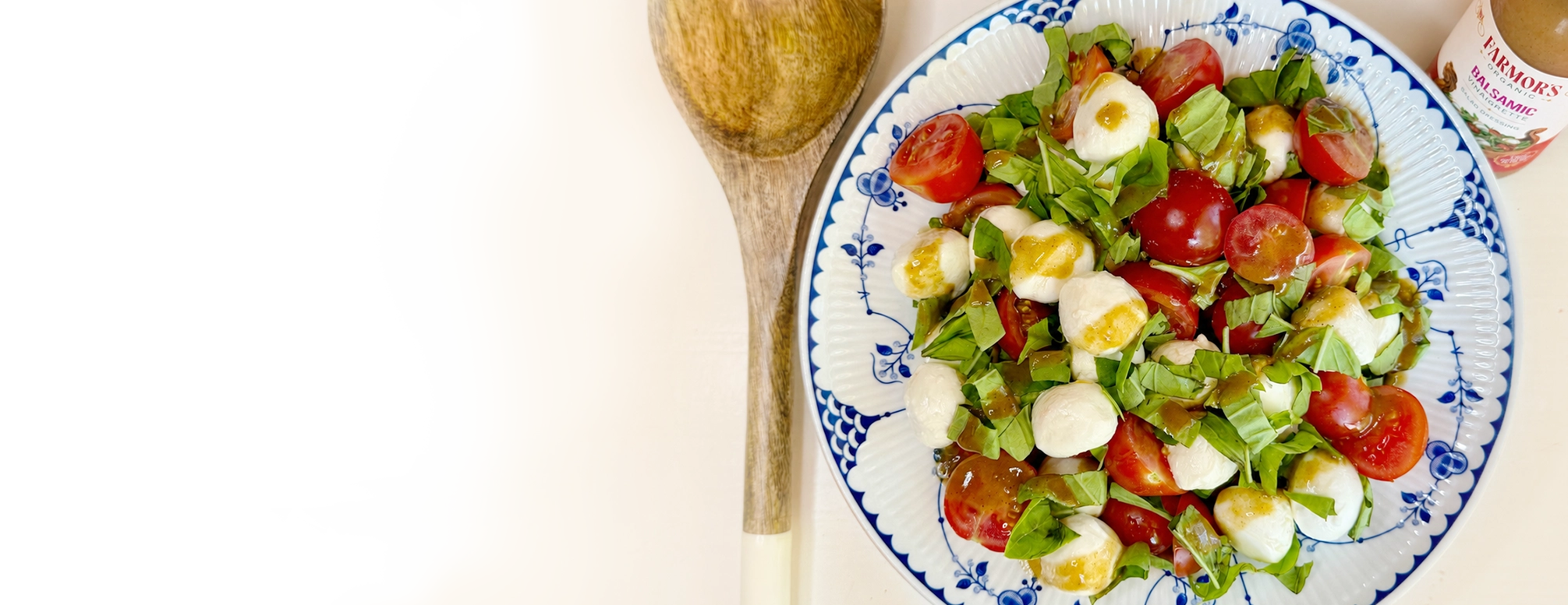 Caprese salad on a blue and white Danish plate, with a wooden serving spoon and a bottle of Farmor’s Balsamic Vinaigrette